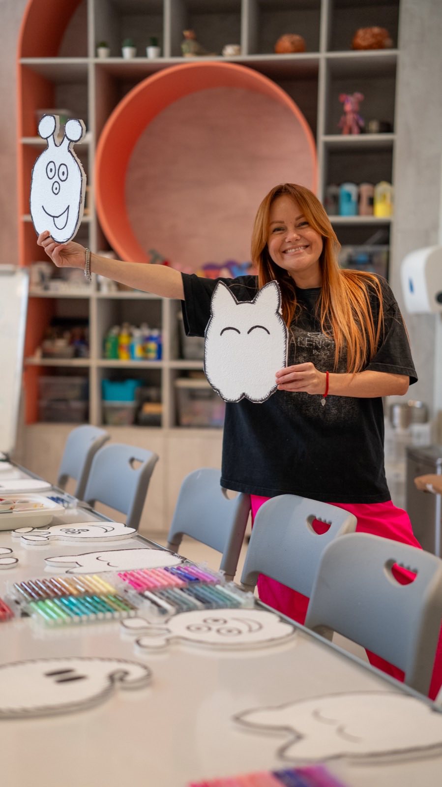 A teacher holding up two foam monster cut-outs in the art room