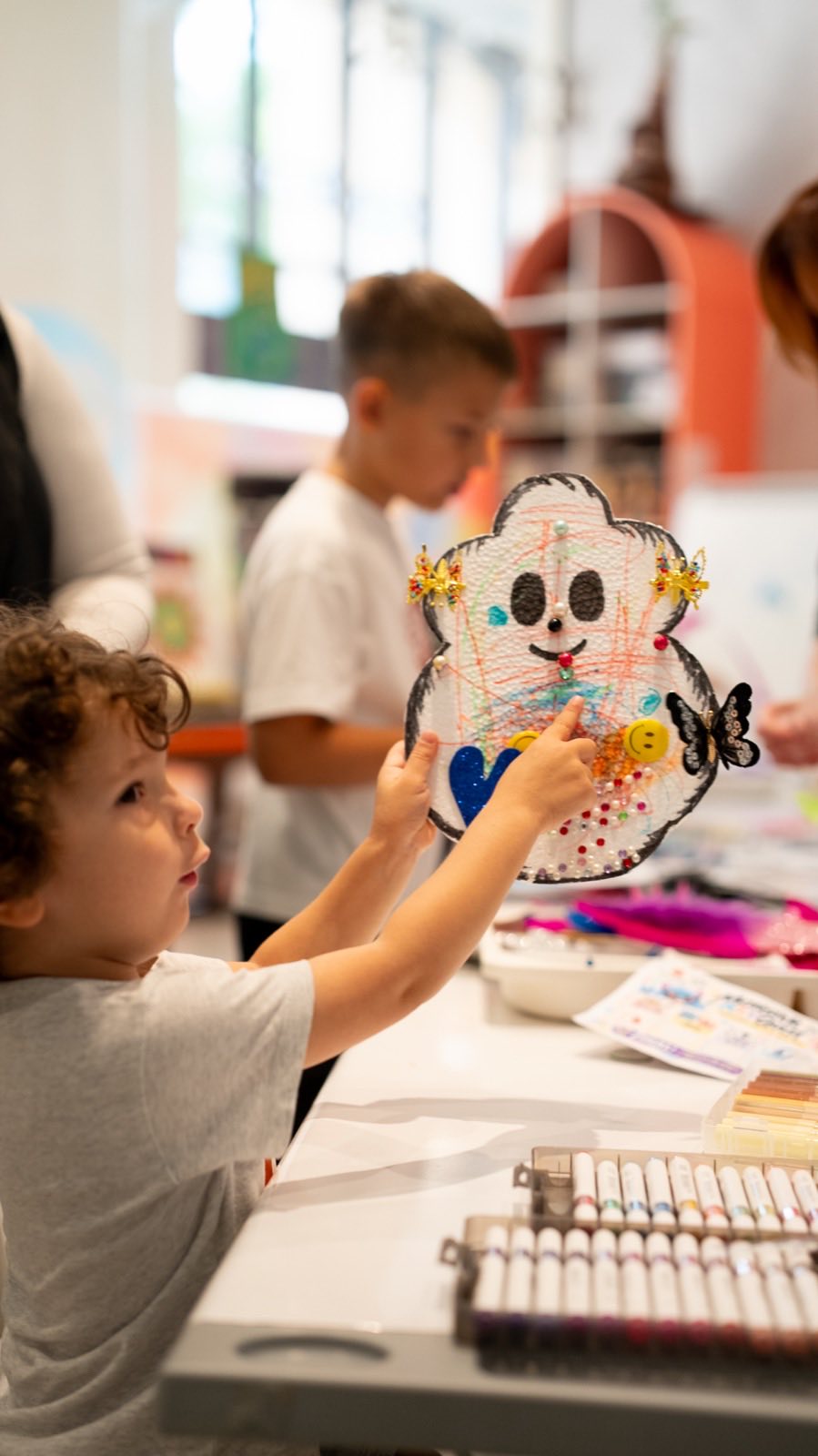 A boy showing the monster he decorated with beads and glitter
