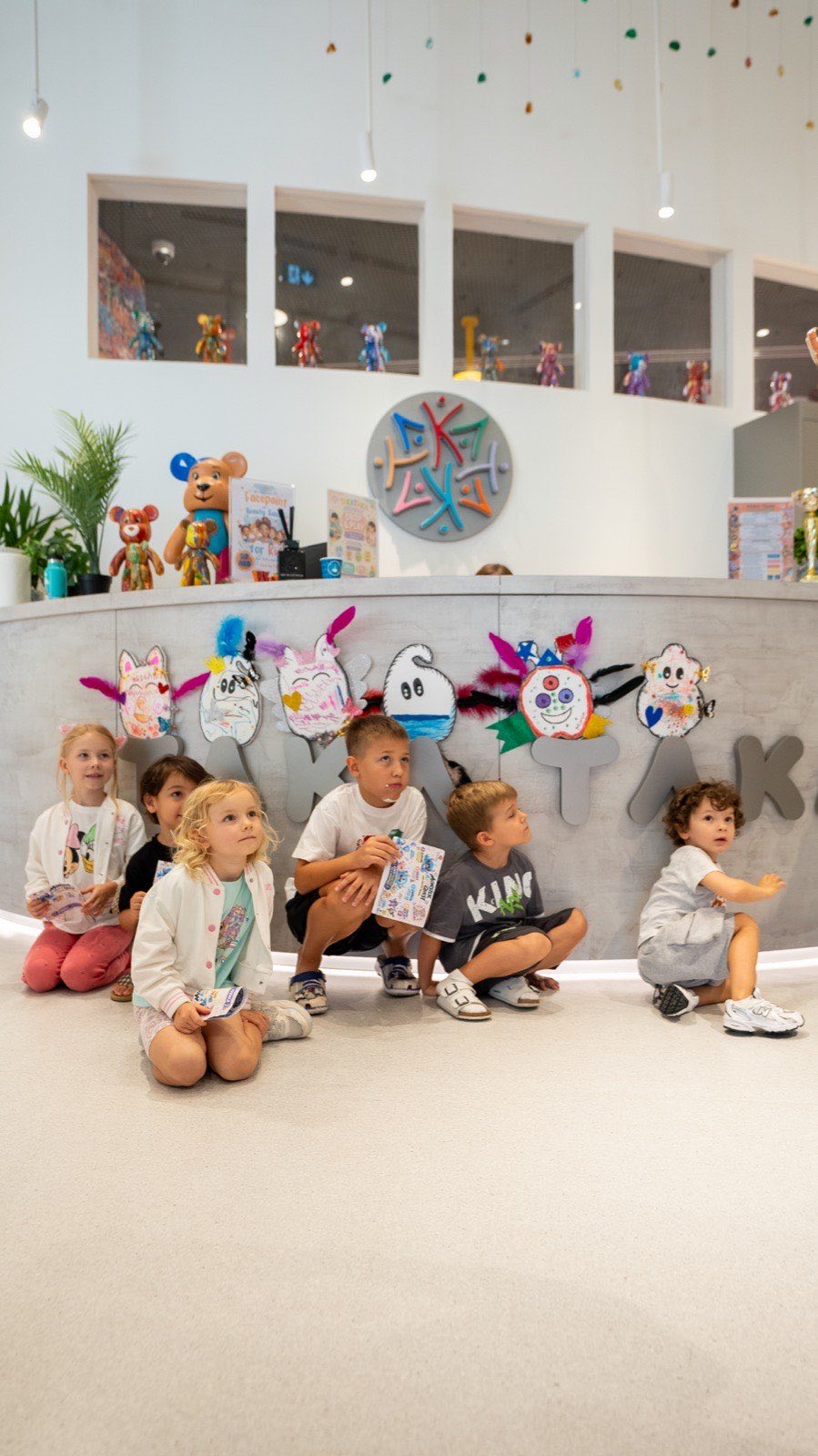 Children sitting under the club sign with their finished monsters on the wall